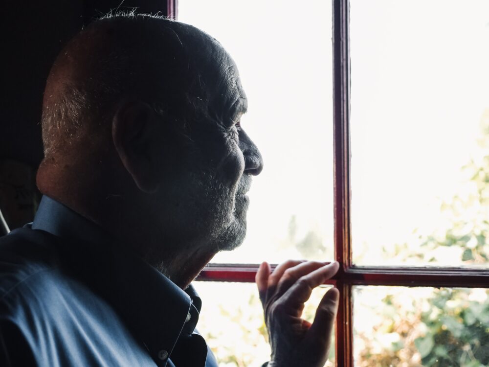 Older adult male looking wistfully out a window